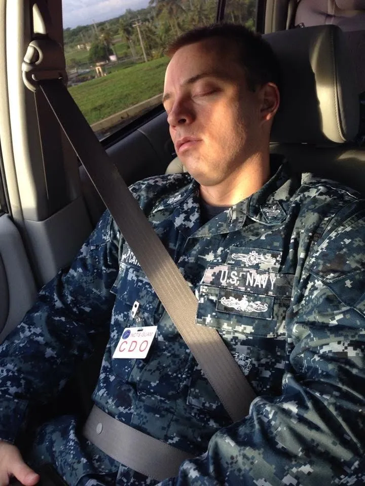 Oliver asleep sitting up in a car, seatbelt on, in his blue Navy working uniform.