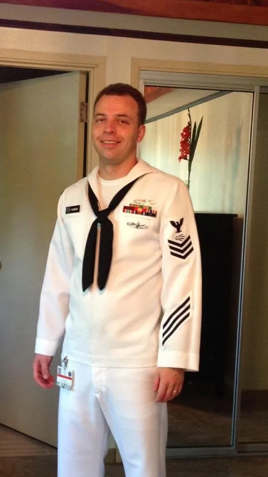 Oliver Carlin in U.S. Navy dress whites, smiling, in an indoor portrait.