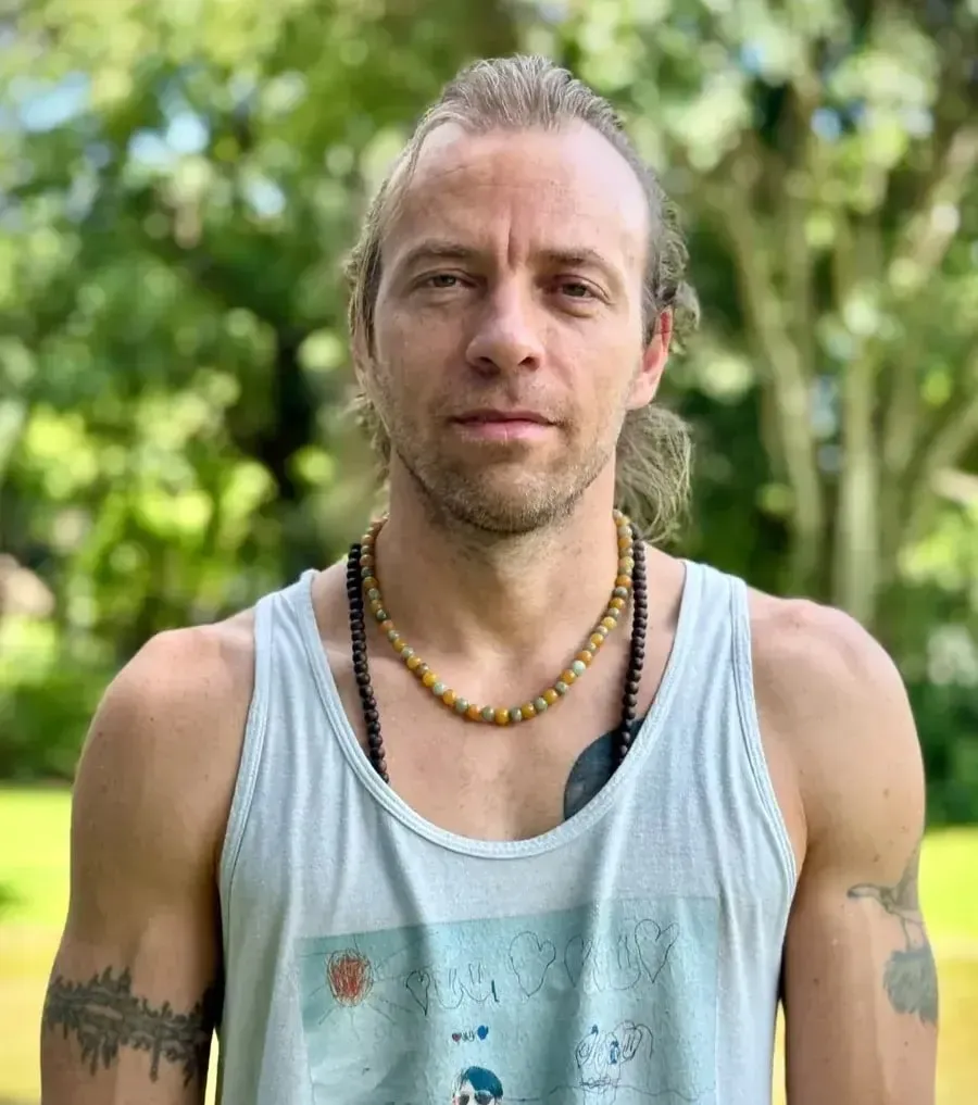Portrait of Oliver Carlin outdoors, in a grey tank top, trees behind him.