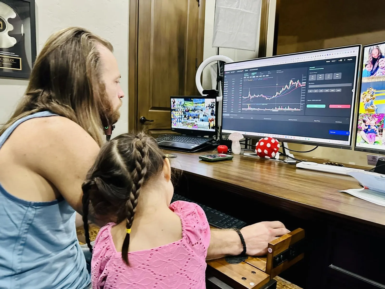 Oliver at his home desk, a chart on the monitor, his daughter sitting beside him.